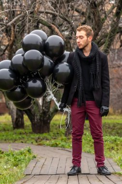 2015.11.22, Moskova, Rusya. Doğum günü hüzünlü bir tatil konseptidir. Siyah atkı ve ceket giyen genç sarışın bir adam elinde siyah balonlar ve başka yöne bakıyor..