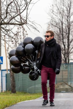 2015.11.22, Moskova, Rusya. Doğum günü hüzünlü bir tatil konseptidir. Siyah fularlı ve ceketli genç sarışın bir adam elinde siyah balonlarla caddeden aşağı doğru gidiyor..