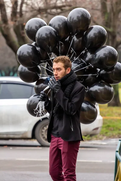 2015.11.22, Moscow, Russia. birthday is a sad holiday concept. A young blonde man wearing black scarf and coat guy holding black balloons and smoking.