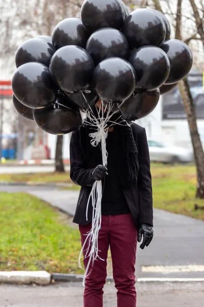 2015.11.22, Moscow, Russia. birthday is a sad holiday concept. A young man wearing black scarf and coat hiding behind black balloons, blur and grain effect.