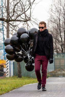 2015.11.22, Moskova, Rusya. Doğum günü hüzünlü bir tatil konseptidir. Siyah fularlı ve ceketli genç sarışın bir adam elinde siyah balonlarla caddeden aşağı doğru gidiyor..