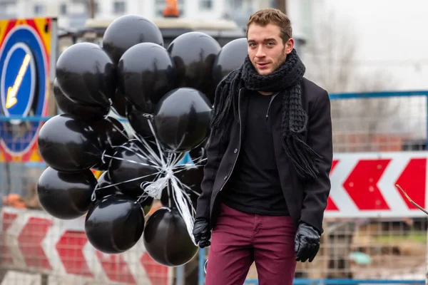 2015.11.22, Moscow, Russia. birthday is a sad holiday concept. A young man wearing black scarf and coat holding black balloons on background of urban scene, blur and grain effect.