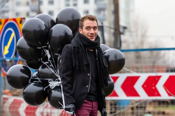 2015.11.22, Moscow, Russia. birthday is a sad holiday concept. A young man wearing black scarf and coat holding black balloons on background of urban scene, blur and grain effect.