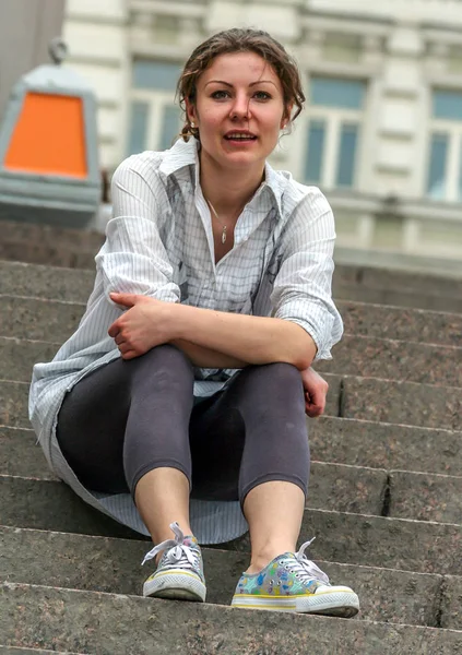 2011.05.21, Moscow, Russia. A young woman wearing white shirt looking sitting on the stone staircase.