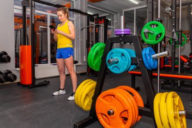 09.02.2020, Maloyaroslavets, Russia. girl in a yellow topic and blue shorts answers a message on the phone between exercises in a sports club.
