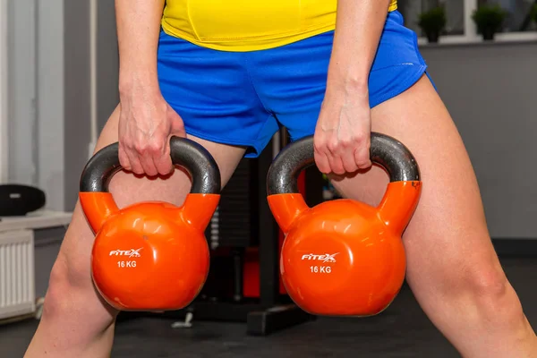 09.02.2020, Maloyaroslavets, Russia. girl in a yellow top and blue shorts does squats with a load. Active lifestyle of modern young woman.