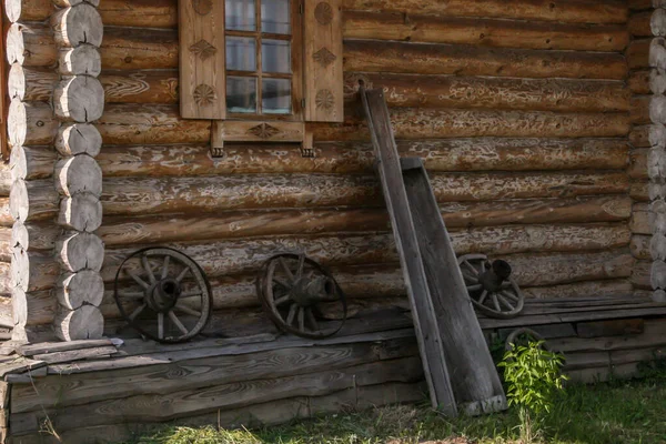 Wall of a rustic log house and wooden cart parts by it, blur and grain effect.