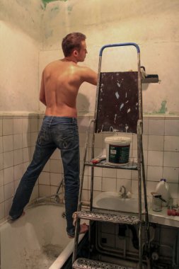 Kot pantolon giyen genç bir adam banyo tamiri yapıyor. Duvara seramik fayanslar koyan bir adam..
