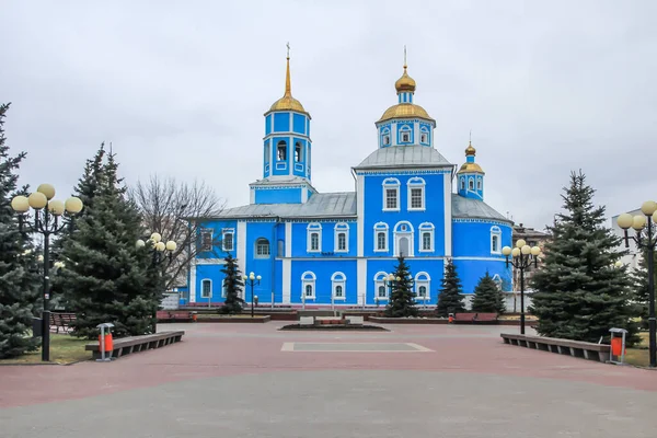 Blue church with golden domes on a square among fir trees. Religious architecture of Russia.