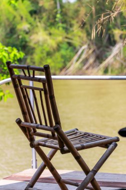 Ormanın ve nehrin arka planındaki kulübenin verandasında bambu sandalyeler.