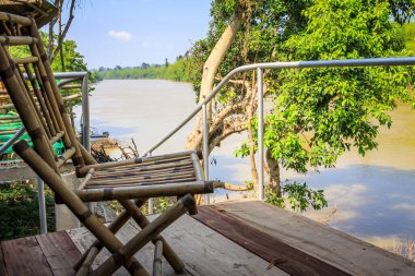 Ormanın ve nehrin arka planındaki kulübenin verandasında bambu sandalyeler.