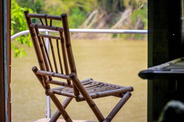 Ormanın ve nehrin arka planındaki kulübenin verandasında bambu sandalyeler.