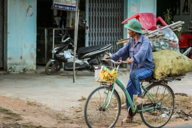 304.2015, Phan Thiet, Vietnam. Ulusal koni şeklinde şapkalı yerel Vietnamlılar yolda bisiklet sürüyor..