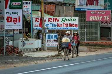 304.2015, Phan Thiet, Vietnam. Ulusal koni şeklinde şapkalı yerel Vietnamlılar yolda bisiklet sürüyor..