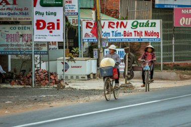 304.2015, Phan Thiet, Vietnam. Ulusal koni şeklinde şapkalı yerel Vietnamlılar yolda bisiklet sürüyor..