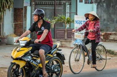 304.2015, Phan Thiet, Vietnam. Ulusal koni şeklinde şapkalı yerel Vietnamlılar yolda bisiklet sürüyor..