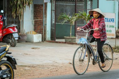 304.2015, Phan Thiet, Vietnam. Ulusal koni şeklinde şapkalı yerel Vietnamlılar yolda bisiklet sürüyor..