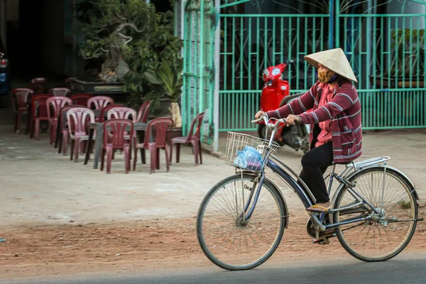 304.2015, Phan Thiet, Vietnam. Ulusal koni şeklinde şapkalı yerel Vietnamlılar yolda bisiklet sürüyor..
