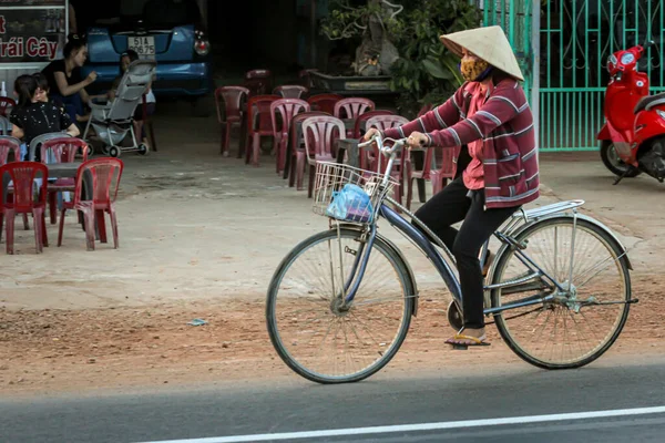 304.2015, Phan Thiet, Vietnam. Ulusal koni şeklinde şapkalı yerel Vietnamlılar yolda bisiklet sürüyor..