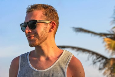 Siyah güneş gözlüklü genç, yakışıklı sakallı adam. Yakından bakıyor.
