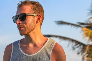 Siyah güneş gözlüklü genç, yakışıklı sakallı adam. Yakından bakıyor.