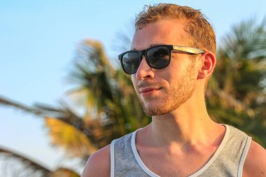 Siyah güneş gözlüklü genç, yakışıklı sakallı adam. Yakından bakıyor.