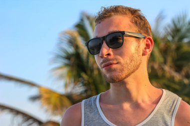 Siyah güneş gözlüklü genç, yakışıklı sakallı adam. Yakından bakıyor.