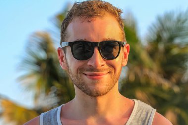 Siyah güneş gözlüklü genç, yakışıklı sakallı adam kameraya bakıyor.