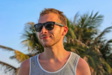 Siyah güneş gözlüklü genç, yakışıklı sakallı adam. Yakından bakıyor.