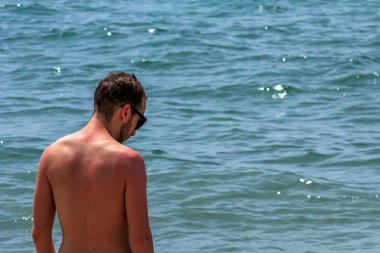 Genç, yakışıklı, sakallı bir adam denizden çıkıp sahile gelmiş.