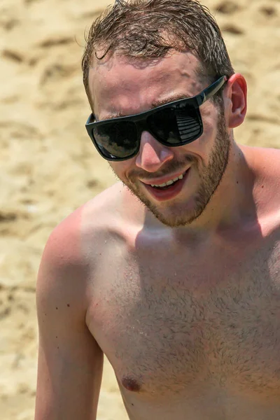 Siyah güneş gözlüklü genç, yakışıklı sakallı adam kameraya bakıyor.