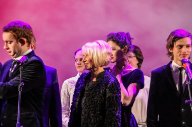 23.01.2012, Moskova, Rusya. Konserin sunucusu (Vera Gorislavovna Tariverdieva) sahnede sahne sanatçılarının arka planında duruyor. Soundtrack ve diğer müziklerin konseri.