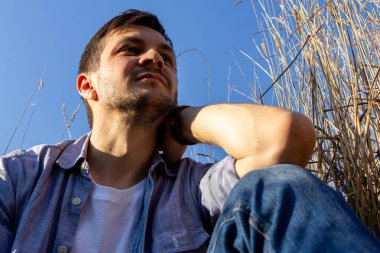 Kot pantolon, beyaz tişört ve mavi gömlek giyen genç çekici bir adam mısır gevreği tarlasında yatar ve yukarı bakar..