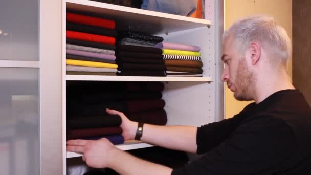 Een Blonde Vent Vouwt Een Stapel Shirts Truien Planken Kast — Stockvideo