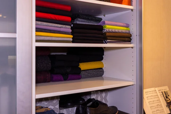 piles of multi-colored t-shirts on a shelf in wardrobe. neatly laid out clothes in the closet.