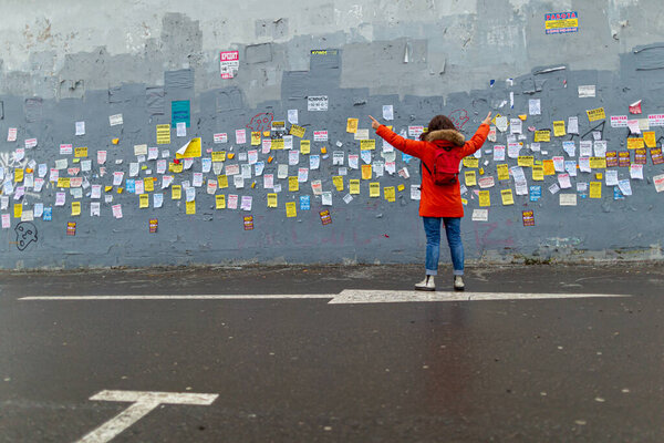 18.11.2018, Москва, Россия. Молодая женщина в красной куртке стоит у стены с многочисленными объявлениями
.