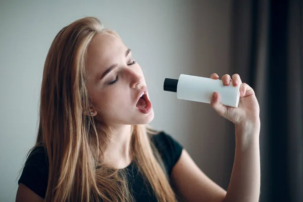 Pretty young woman sing and hold two bottle with empty space. Shampoo and conditioner.