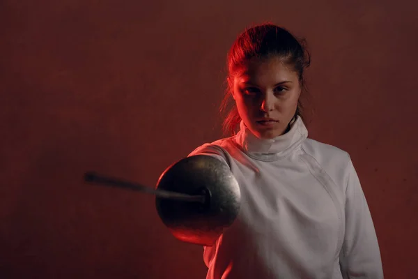 Fencer woman portrait with fencing sword in red light.