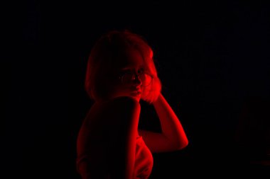 İç çamaşırlı genç bir kadın kırmızı arka ışıkta poz veriyor.