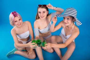 Mavi arka planda yalıtılmış mayo giymiş üç genç kadın.