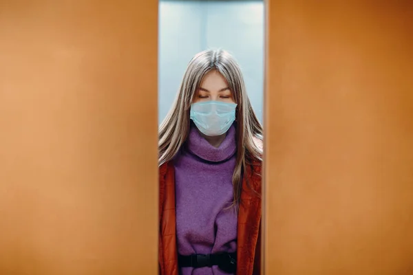 Young woman with closed eyes standing in elevator in medical mask. Doors are closing. Coronavirus COVID-19 pandemic concept.