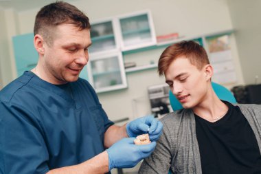 Diş hekimliği. Diş hekimi hastaya implantlar gösteriyor. Diş Kliniği.