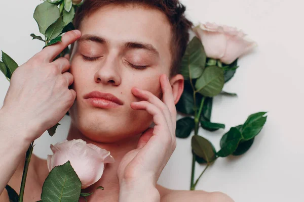 Young male model with flowers. Beauty portrait. Touching fresh smooth skin.