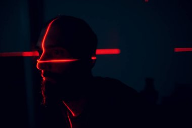 Yüzü kırmızı lazerle aydınlatılmış, karanlıkta bir adam var.