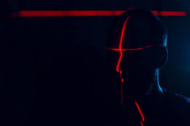 Yüzü kırmızı lazerle aydınlatılmış, karanlıkta bir adam var.