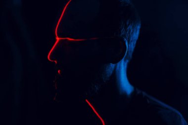 Yüzü kırmızı lazerle aydınlatılmış, karanlıkta bir adam var.