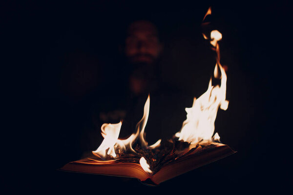 Man holds burning book in his hands.