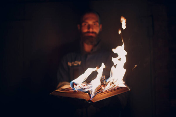 Man holds burning book in his hands.