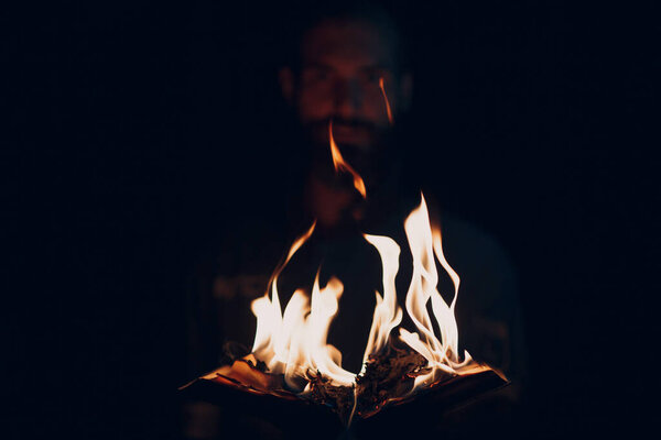 Man holds burning book in his hands.