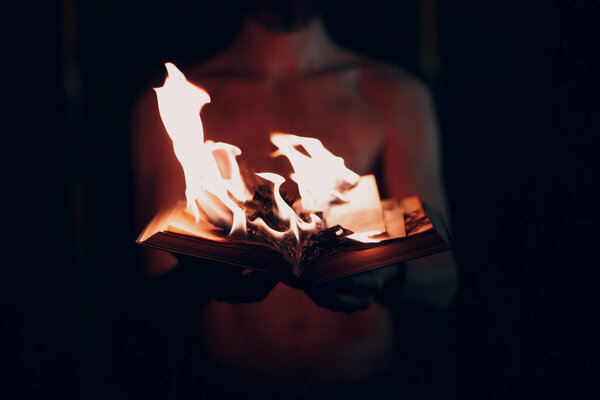 Man holds burning book in his hands.